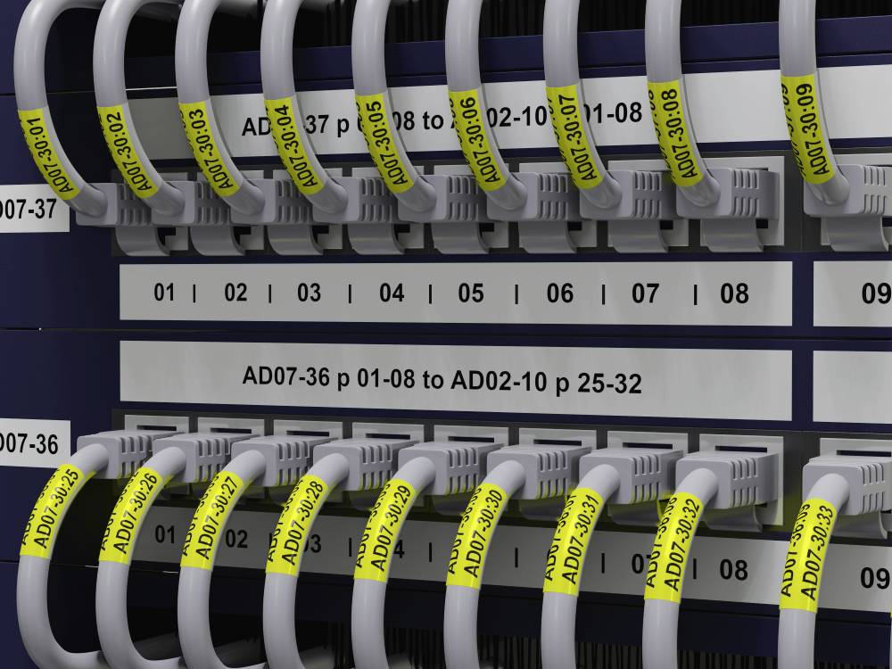 Netzwerkverkabelung mit nummerierten grauen Kabeln in einem Serverrack. Gelbe Etiketten erleichtern die Identifikation der Ports.