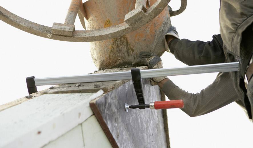 Eine Person bedient eine Betonrutsche, um Beton in eine Form zu gießen. Ein Schraubzwinge hält die Form zusammen.