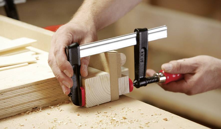 Eine Person verwendet eine Zwinge, um zwei Holzstücke auf einer Werkbank sicher zusammenzuhalten.