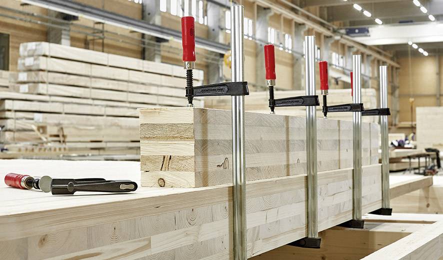 Holzwerkstatt: Stapel von Holzbalken, mit Metallzwingen zusammengehalten, bereit zur Bearbeitung in einer industriellen Umgebung.