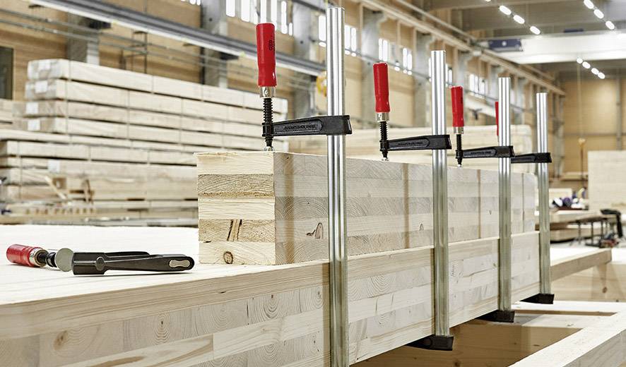 Holzwerkstatt mit Holzblöcken, die mit Klemmen befestigt sind. Im Hintergrund sind weitere Holzstapel zu sehen.