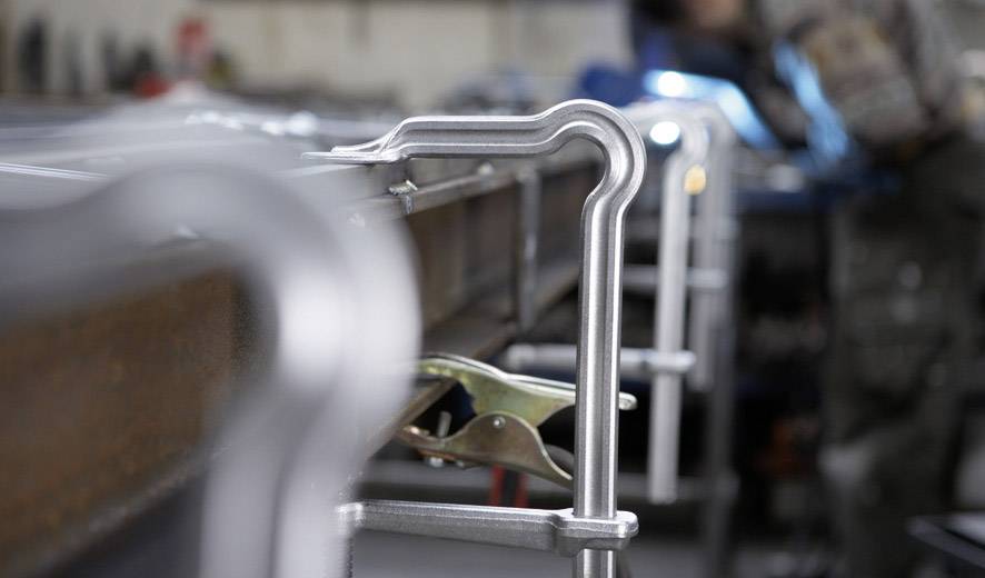 Vordergrund zeigt Metall-Klemmen, unscharfer Hintergrund mit Werkstatt-Umgebung. Fokus auf Handwerksarbeit.