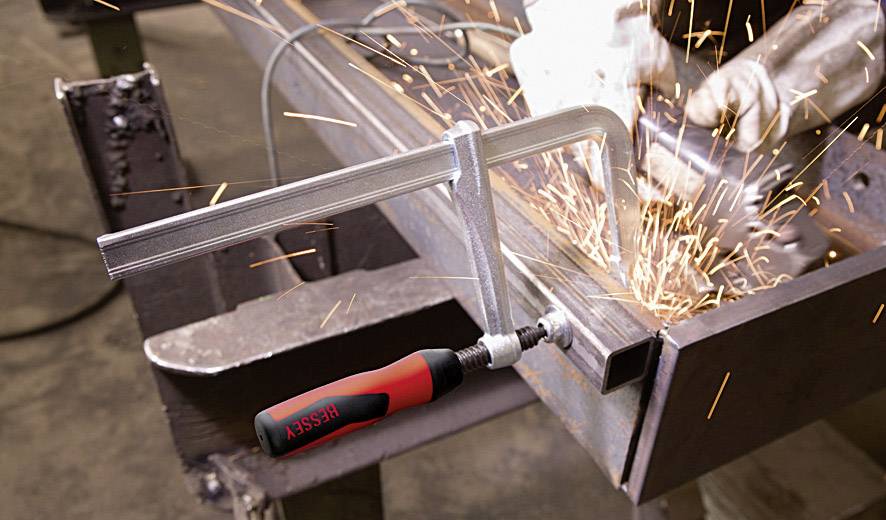 Ein Handwerker schleift Metall mit einem Winkelschleifer, während Funken fliegen. Ein Schraubstock hält das Werkstück sicher.