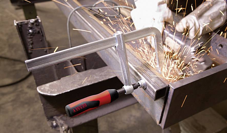 Eine Metallklemme hält ein Werkstück, während ein Arbeiter mit einer Flex Funken sprüht.