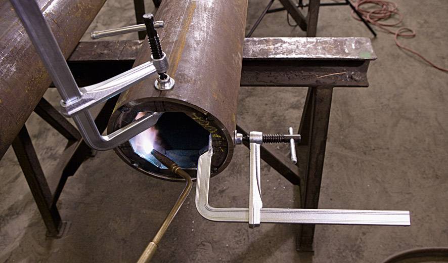 Eine Metallrundung wird mit Schweißklemmen fixiert, während eine Flamme im Inneren des Rohrs sichtbar ist.