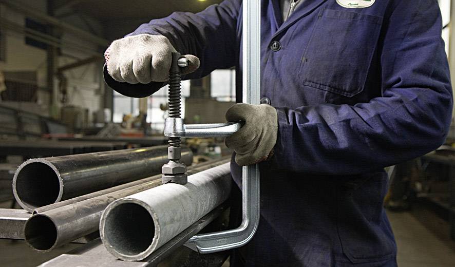 Eine Person in blauer Arbeitskleidung bearbeitet Metallrohre mit einem Schraubstock in einer Werkstattumgebung.