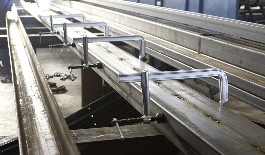Metallträger wird mit mehreren C-Klemmen auf einer Werkbank fixiert.