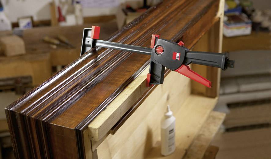 Holzregal in Werkstatt wird mit Zwinge fixiert. Flasche Leim im Hintergrund.