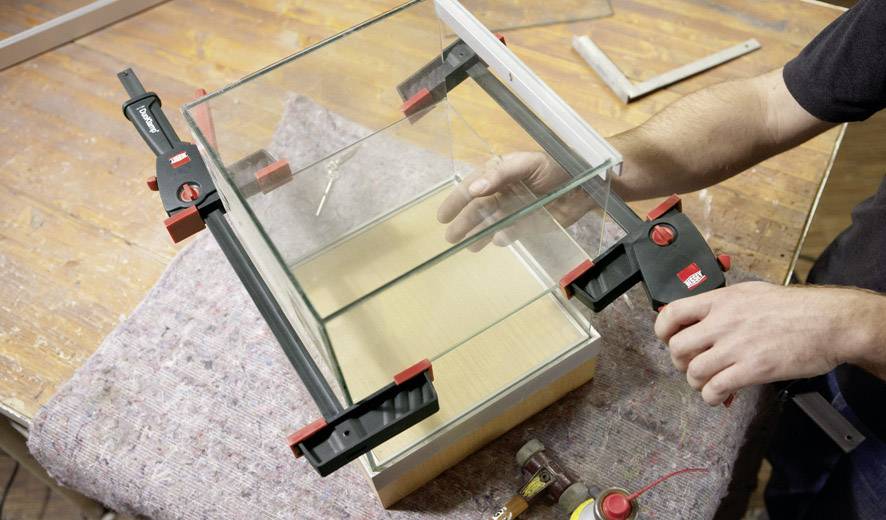 Eine Person baut ein Glasgehäuse, wobei sie zwei große schwarze Klemmen verwendet, um die Glasscheiben zusammenzuhalten.