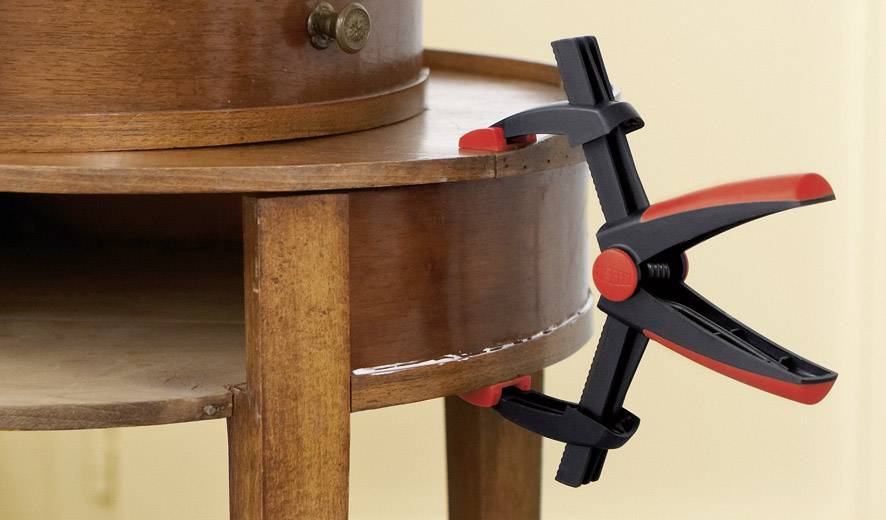 Holztisch-Ecke mit zwei roten und schwarzen Klemmen befestigt, um die Stabilität während der Trocknung von Klebstoff zu gewährleisten.