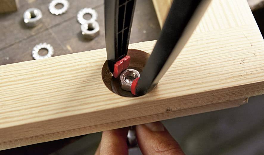 Nahaufnahme eines Holzrahmens, in den eine Mutter mit einem Schraubenschlüssel eingesetzt wird. Hände richten die Mutter aus.