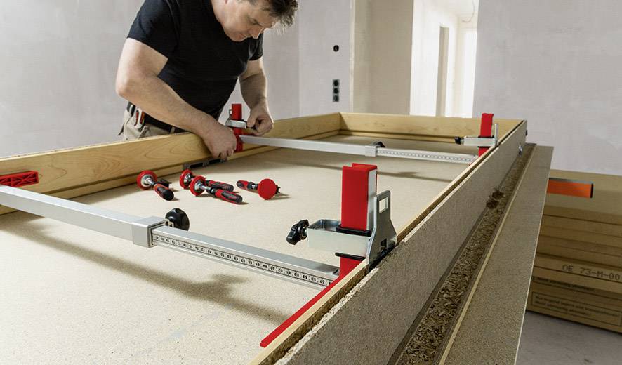 Ein Mann montiert Holzplatten mit Metallwerkzeug auf einem Tisch.
