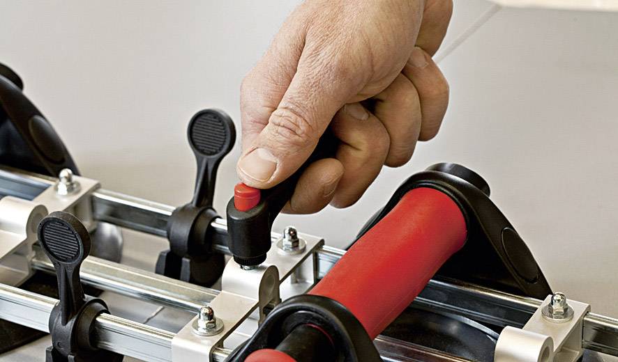 Eine Hand dreht einen Griff an einem Gerät mit Hebelmechanismus und Metallstangen, möglicherweise zur Einstellung oder Fixierung.