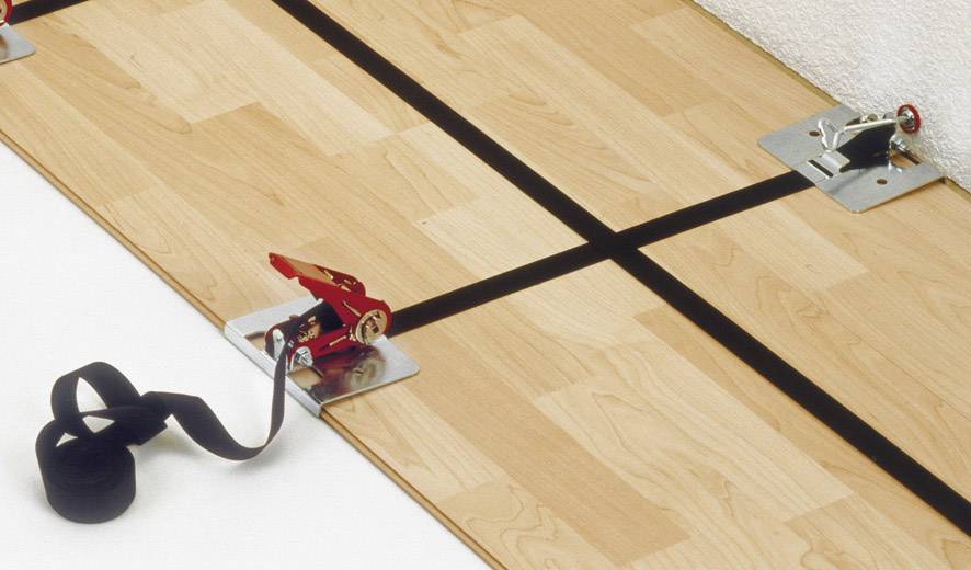 Ein Holzfußboden wird mit Spanngurten und Metallecken verbunden, um eine stabile Verbindung zwischen den einzelnen Paneelen zu gewährleisten.