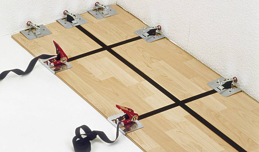 Mehrere Spanngurte sind an Metallplatten auf einem Laminatboden befestigt, um sicherzustellen, dass die Platten gut verlegt sind.