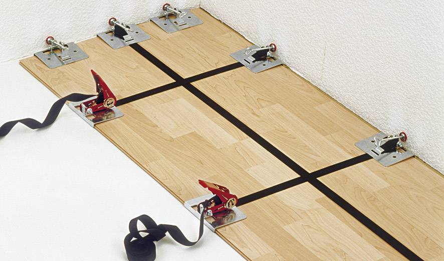 Holzboden wird mit Metallklammern verlegt. Die Klammern halten die Planken zusammen während der Installation an der Wand.