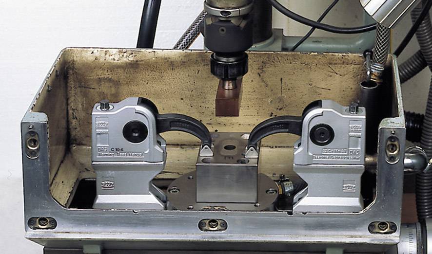 Metallbearbeitungsmaschine mit kastenförmigem Gehäuse und zwei Halterungen für präzise Verarbeitung. Zentrales Bohrwerkzeug sichtbar.