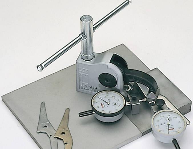 Manometers auf einer Metallplatte zur Messung von Druck. Daneben liegen Metallteile und ein Hebel, die zur Unterstützung der Messung dienen.