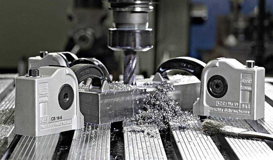 Eine Fräsmaschine bearbeitet ein Metallstück, umgeben von vier Magnetspannern, mit Metallspänen auf einem maschinellen Arbeitstisch.
