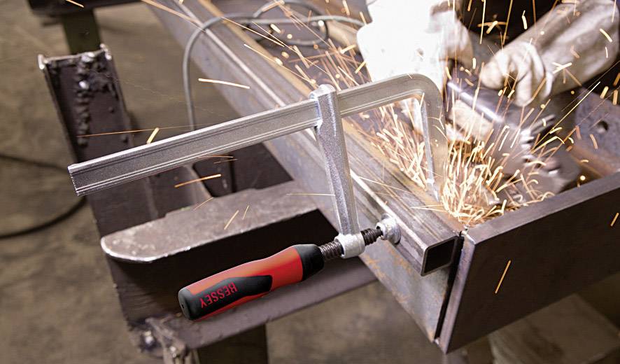 Funken sprühen beim Schleifen eines Metallteils, das von einer Klemme gehalten wird. Ein Schraubenzieher liegt unbenutzt daneben.
