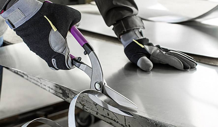 Eine Person schneidet präzise Metallblech mit einer Metallschere. Die Person trägt Schutzhandschuhe.