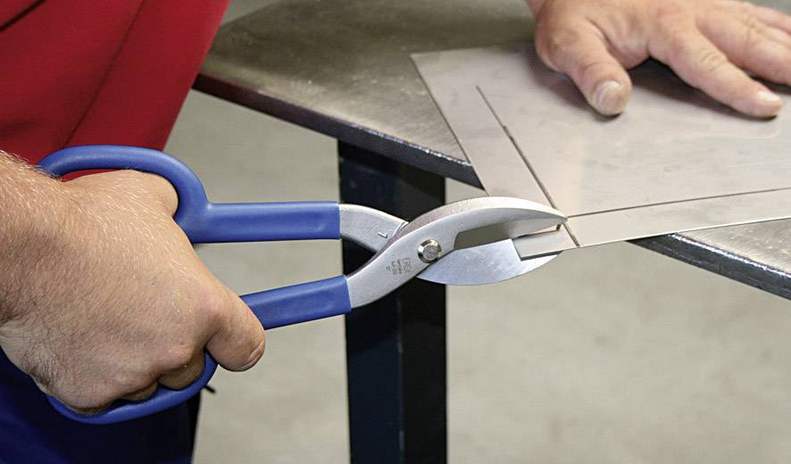 Eine Person schneidet mit einer blauen Metallschere ein Stück Blech. Die Schere bearbeitet präzise das Metall.