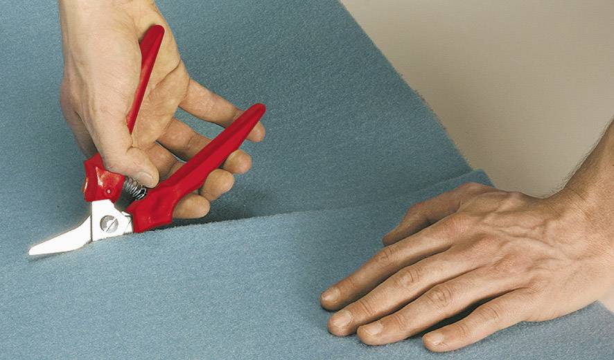Zwei Hände arbeiten mit einer roten Schere, um blauen Stoff zu schneiden.