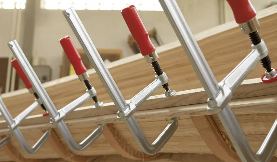 Holzzwingen mit roten Griffen halten mehrere Holzplatten in einer Werkstatt zusammen.
