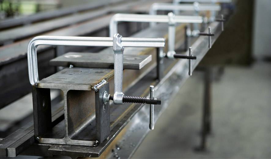 Mehrere C-Klammern befestigen Metallträger auf einem Tisch in einer Werkstatt.