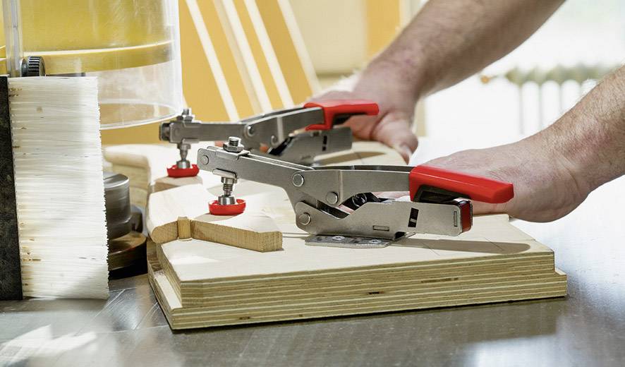 Person bedient eine Holzbearbeitungsmaschine mit roten Griffen. Holz wird mit Spannvorrichtungen fixiert.