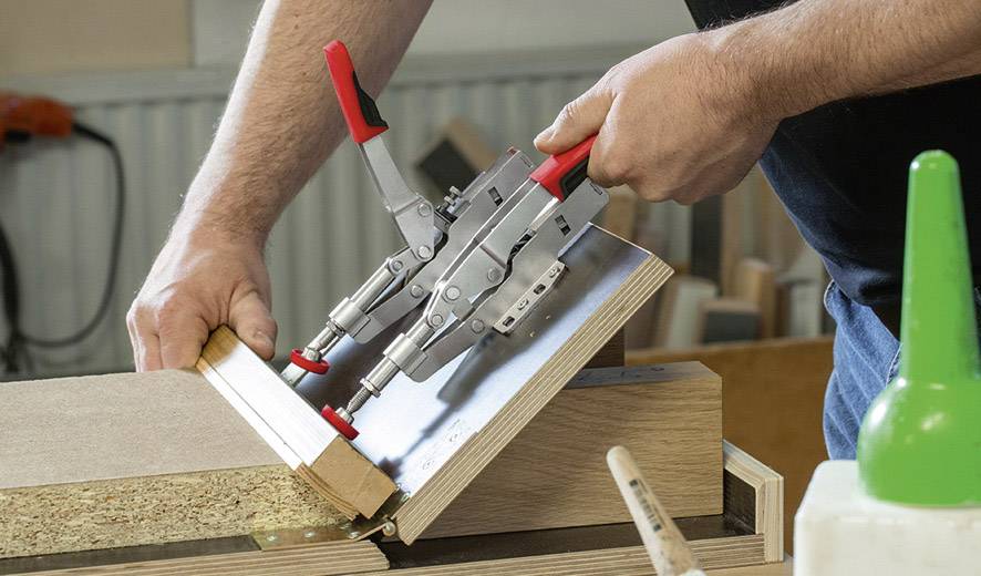 Eine Person justiert Holzplatten mit metallischen Klemmen in einer Werkstatt, um eine stabile Verbindung zu schaffen.