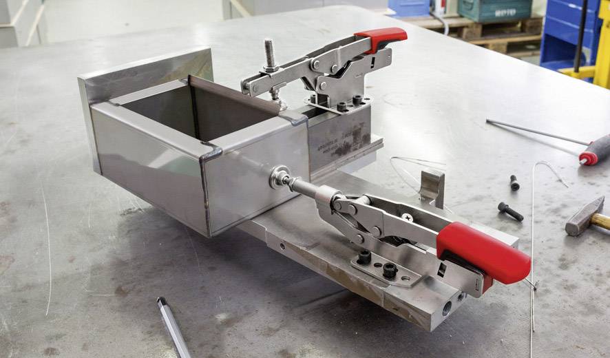 Metallarbeitsstück in industrieller Klemme auf Arbeitstisch, bereit für weitere Bearbeitung; zeigt technische Präzision.