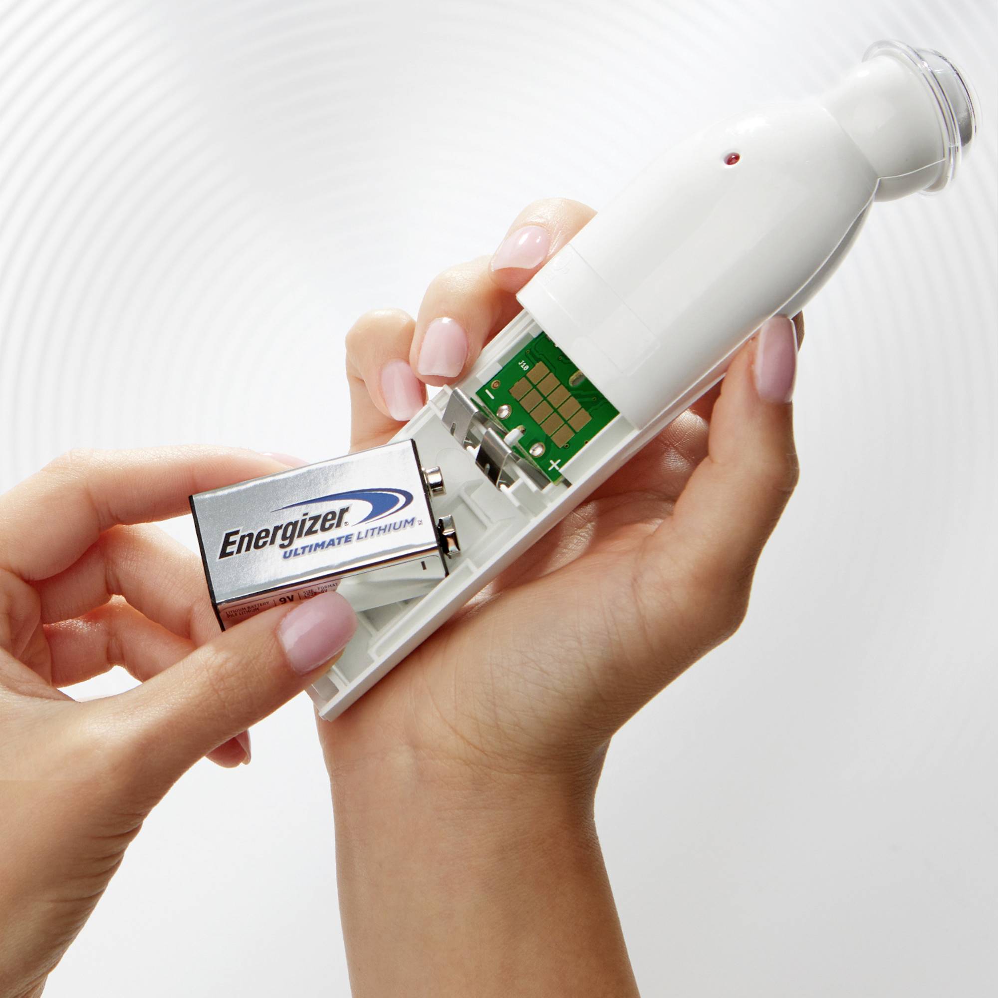 Eine Person hält ein batteriebetriebenes Gerät und setzt eine 'Energizer' Lithium-Batterie ein. Die Hände stützen das Gerät vorsichtig.