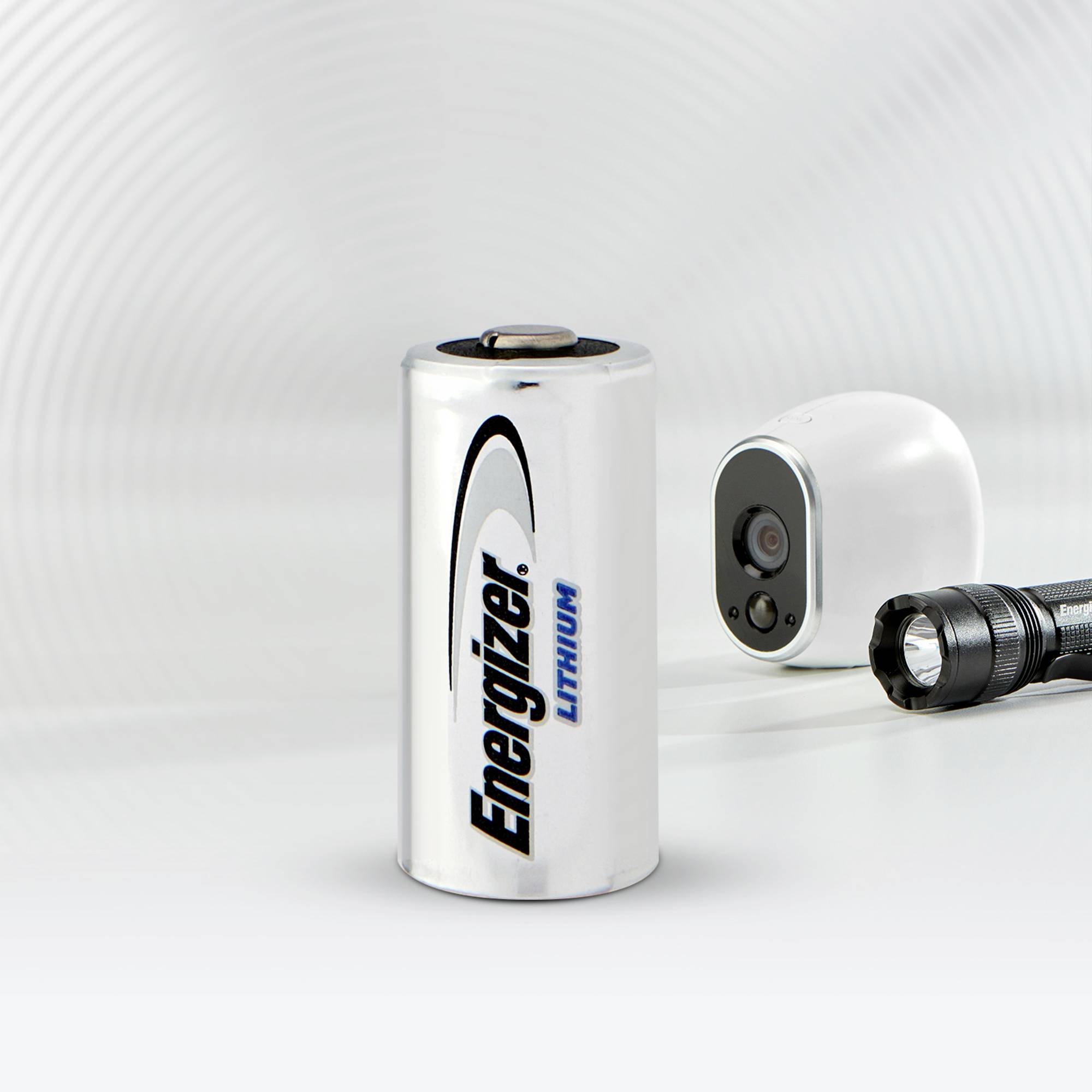 Batterie der Marke Energizer, neben einer kleinen Kamera und Taschenlampe, auf weißem Hintergrund platziert.