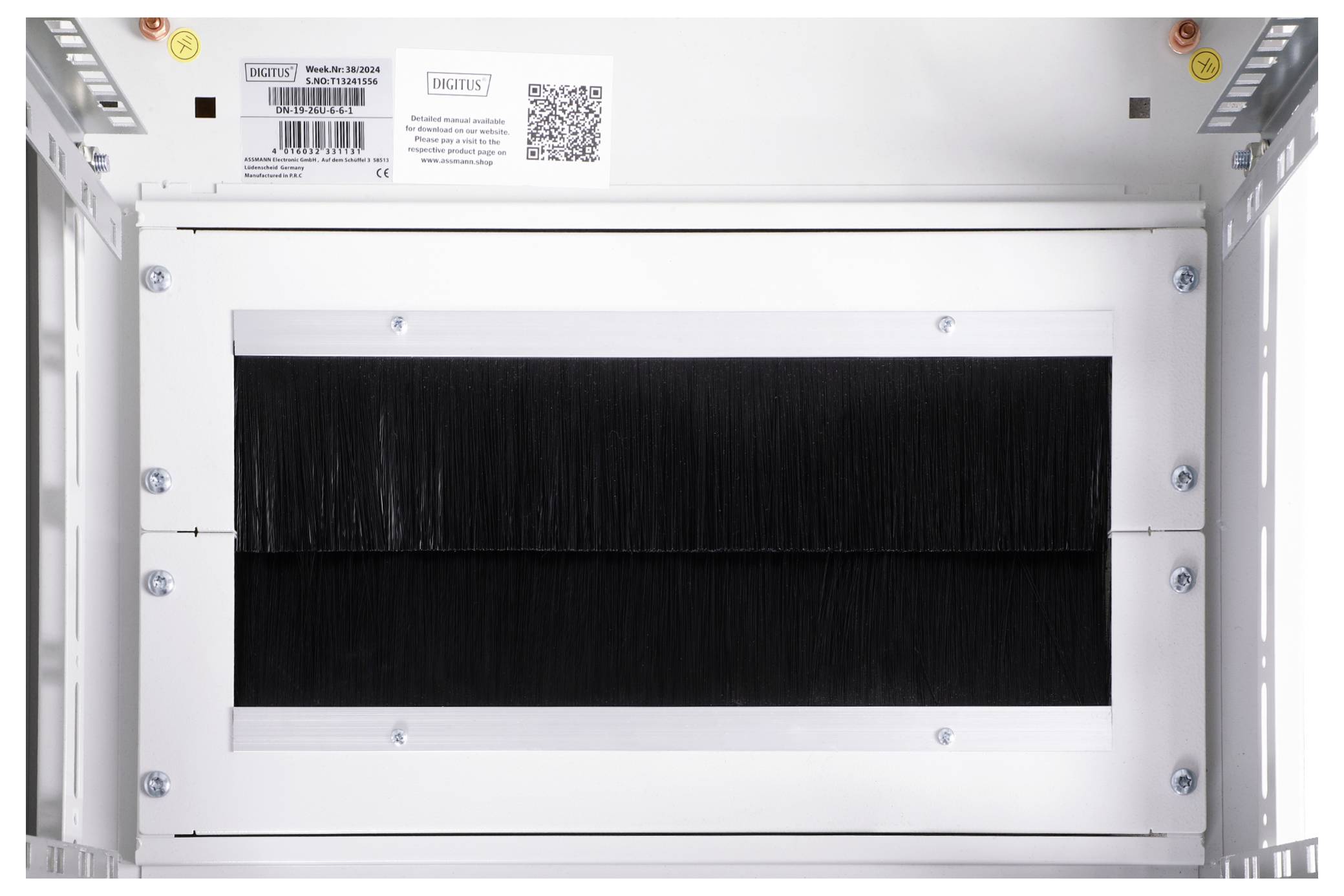 Ein weißes, rechteckiges Gerät mit einer schwarzen Bürstenfläche in der Mitte, eingebaut in einem Metallrahmen mit Etiketten und QR-Code oben.