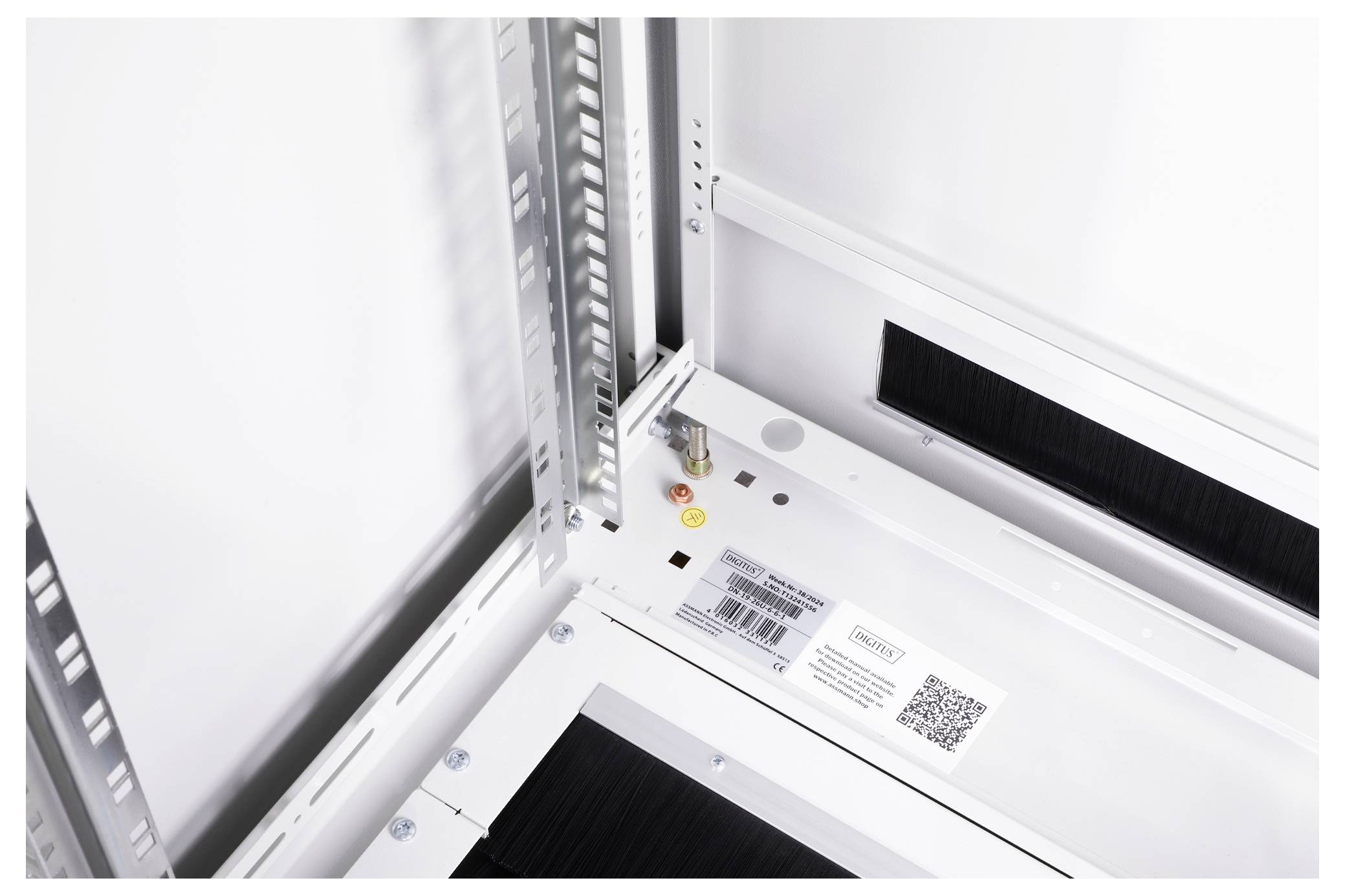 Innenansicht eines metallischen Gehäuses mit elektronischen Komponenten und QR-Code auf einem Etikett. Teile für Kabeldurchführungen sichtbar.