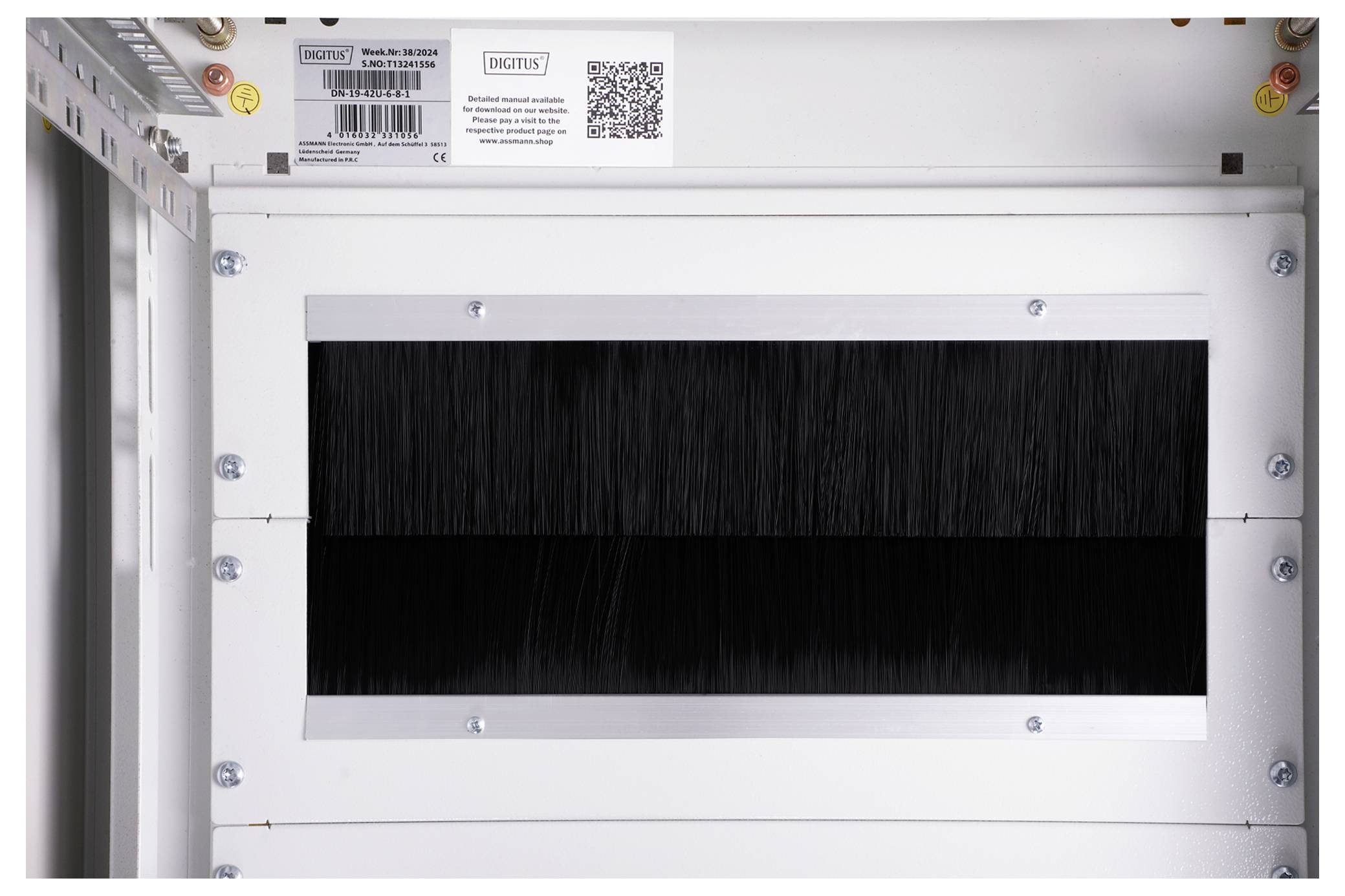 Weiße Industriewand mit rechteckigem Belüftungsgitter. Darüber ein QR-Code und Etikett mit technischer Information und Barcode.