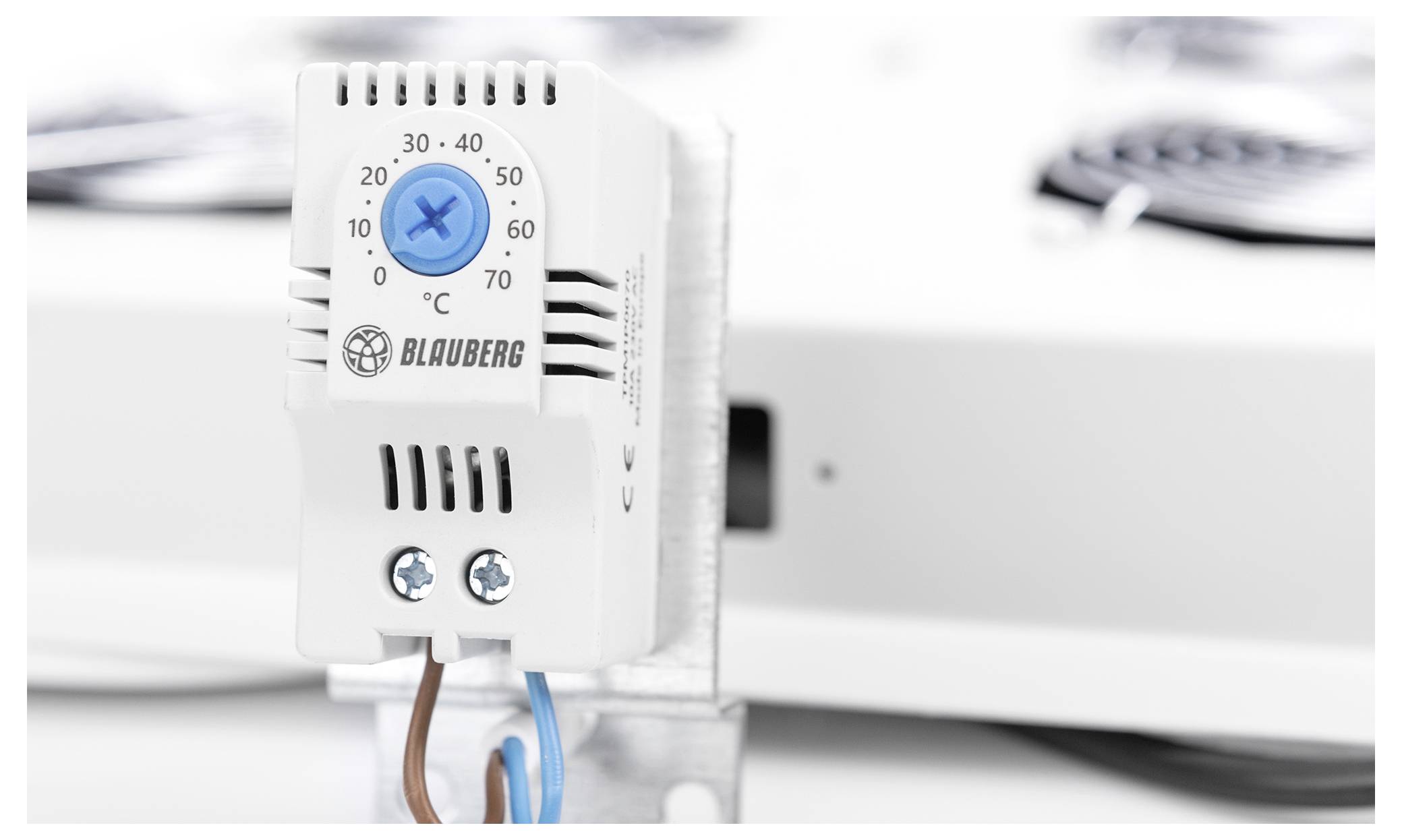 Ein weißes Thermostat mit einer blauen Einstelldrehscheibe ist auf 40°C eingestellt. Es verfügt über das Blauberg-Logo und ist auf einer Metallhalterung mit sichtbarer Verdrahtung montiert.