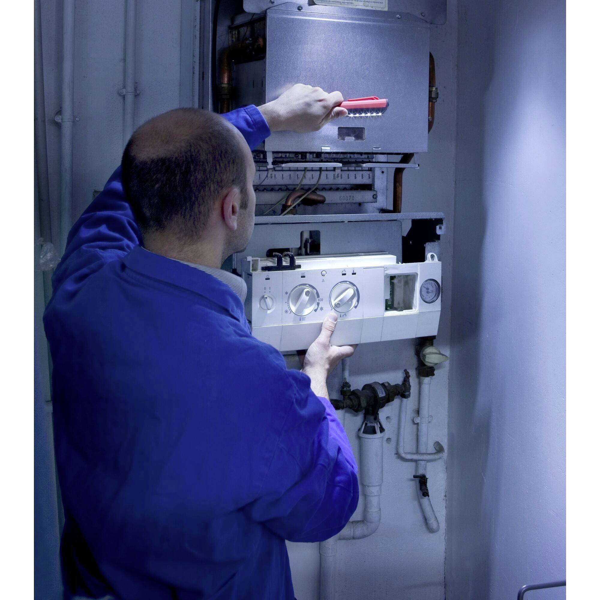 Ein Techniker in blauer Arbeitskleidung arbeitet an einem Heizkessel. Er verwendet einen Schraubendreher und kontrolliert die Einstellungen.