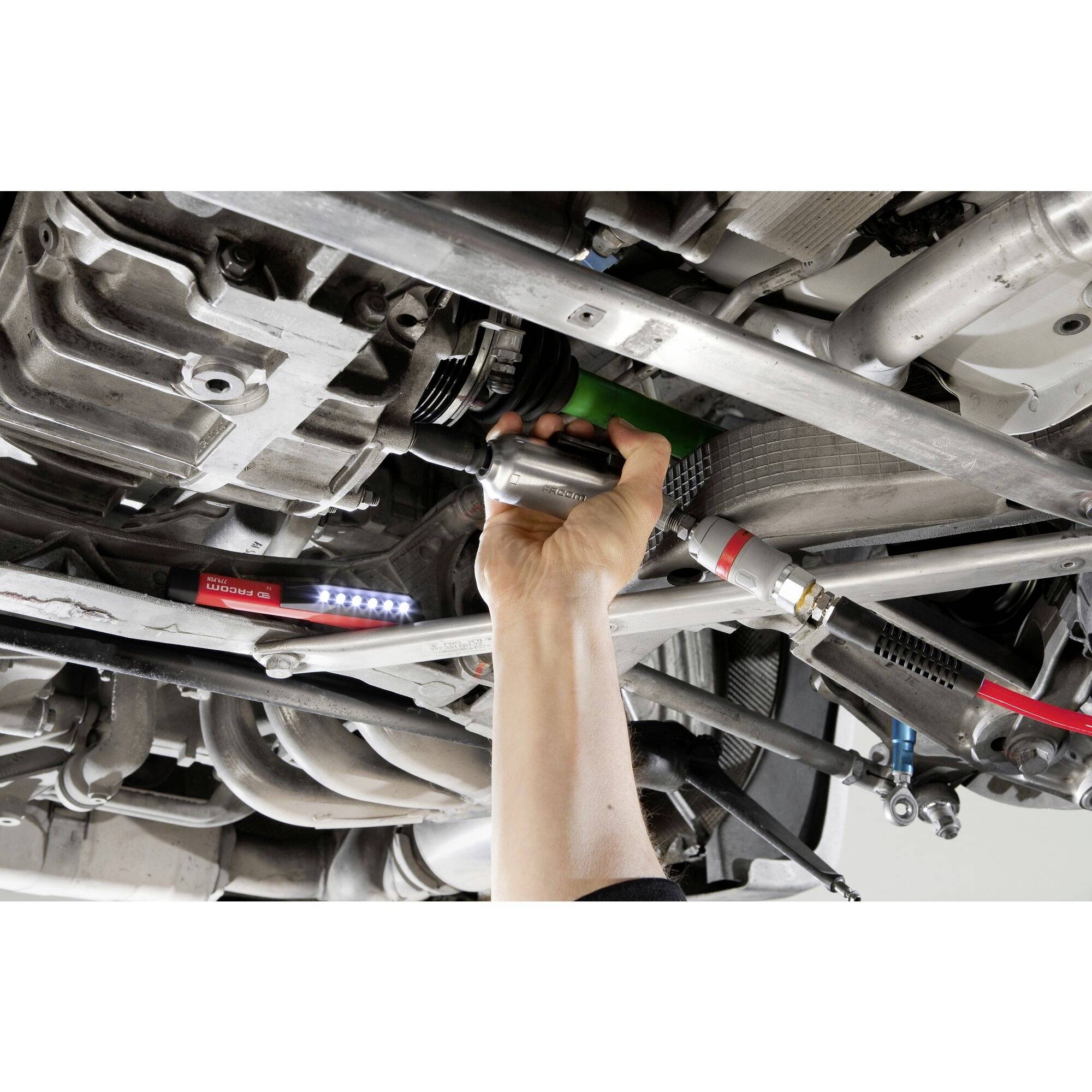 Ein Mechaniker arbeitet unter einem Auto, überprüft den Motorraum und benutzt eine Taschenlampe zum Ausleuchten, gehalten von einer Hand.