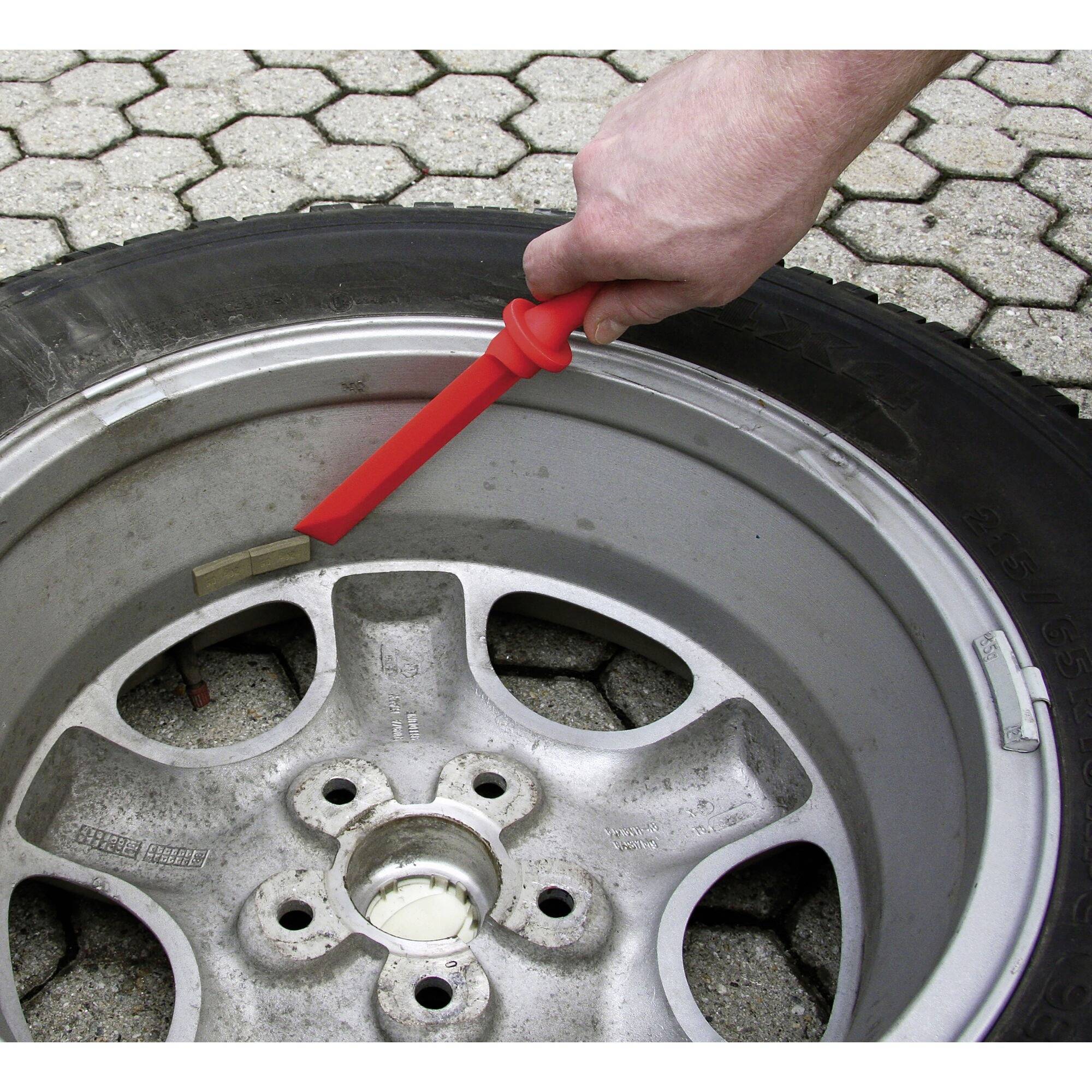 Eine Hand zeigt mit einem roten Marker auf den Rand eines beschädigten Autoreifens auf Kopfsteinpflasterbelag.