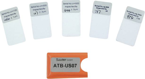 Fünf Prüfkarten mit unterschiedlichen Seriennummern und Messwerten, daneben ein orangefarbenes Gerät mit der Aufschrift 'ATB-US07'.