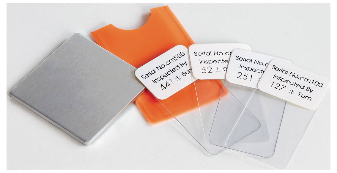 Drei Kartonetiketten mit Seriennummern und Inspektionsinformationen auf transparenten Kunststoffplatten, nebst orangem Etui.