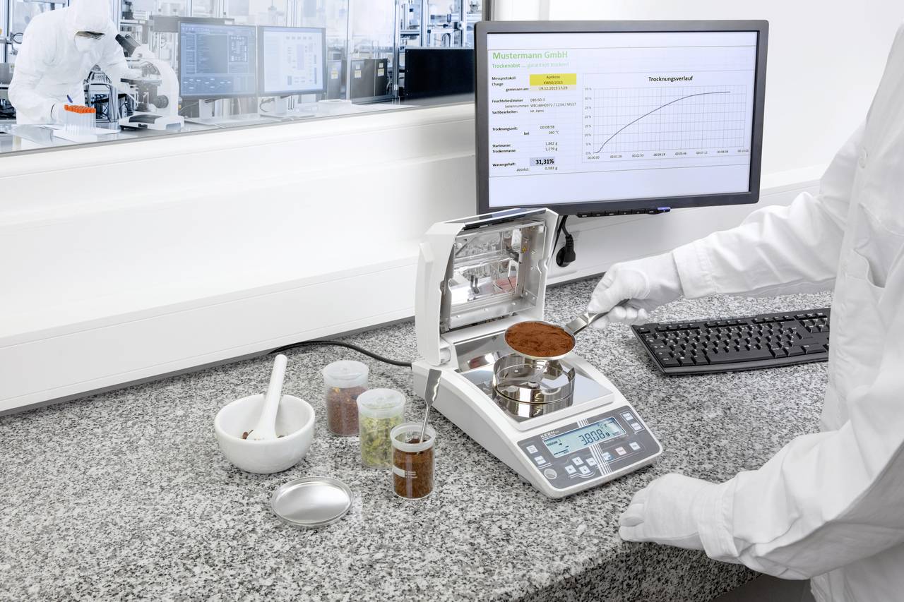 Ein Laborant wiegt eine Substanz auf einer Präzisionswaage. Im Hintergrund ist ein Computerbildschirm mit Daten und Diagramm sichtbar.