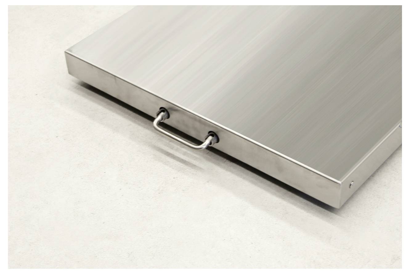 Eine rechteckige silberne Metallplatte mit einem Griff in der Mitte, liegt auf einem hellen Boden.