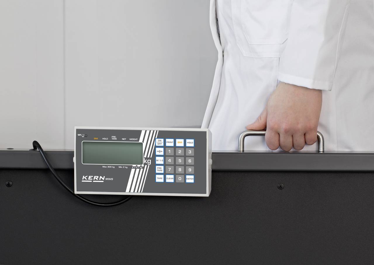 Eine Person in weißem Kittel hält einen schwarzen Koffer an einem Griff. Auf dem Koffer befindet sich ein digitales Display mit Tastenfeld.