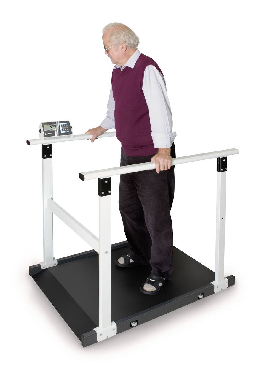 Älterer Mann steht auf einem Laufband mit Haltegriffen, blickt auf ein digitales Display. Die Szene deutet auf Reha-Übungen hin.