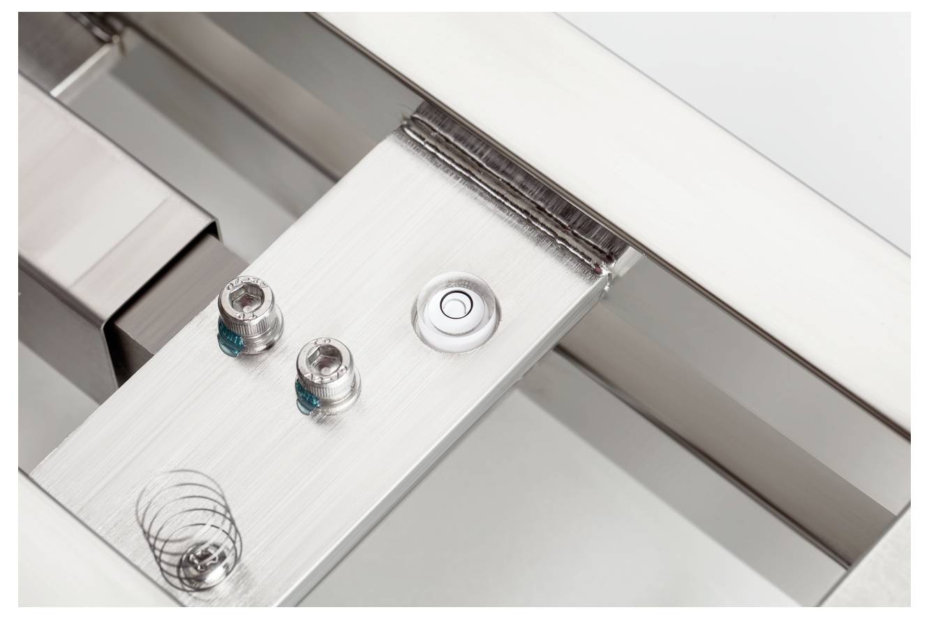 Metallisches Gerät mit zwei Schrauben und einer runden Taste auf einer rechteckigen Metallfläche. Technisches Design in Nahaufnahme.