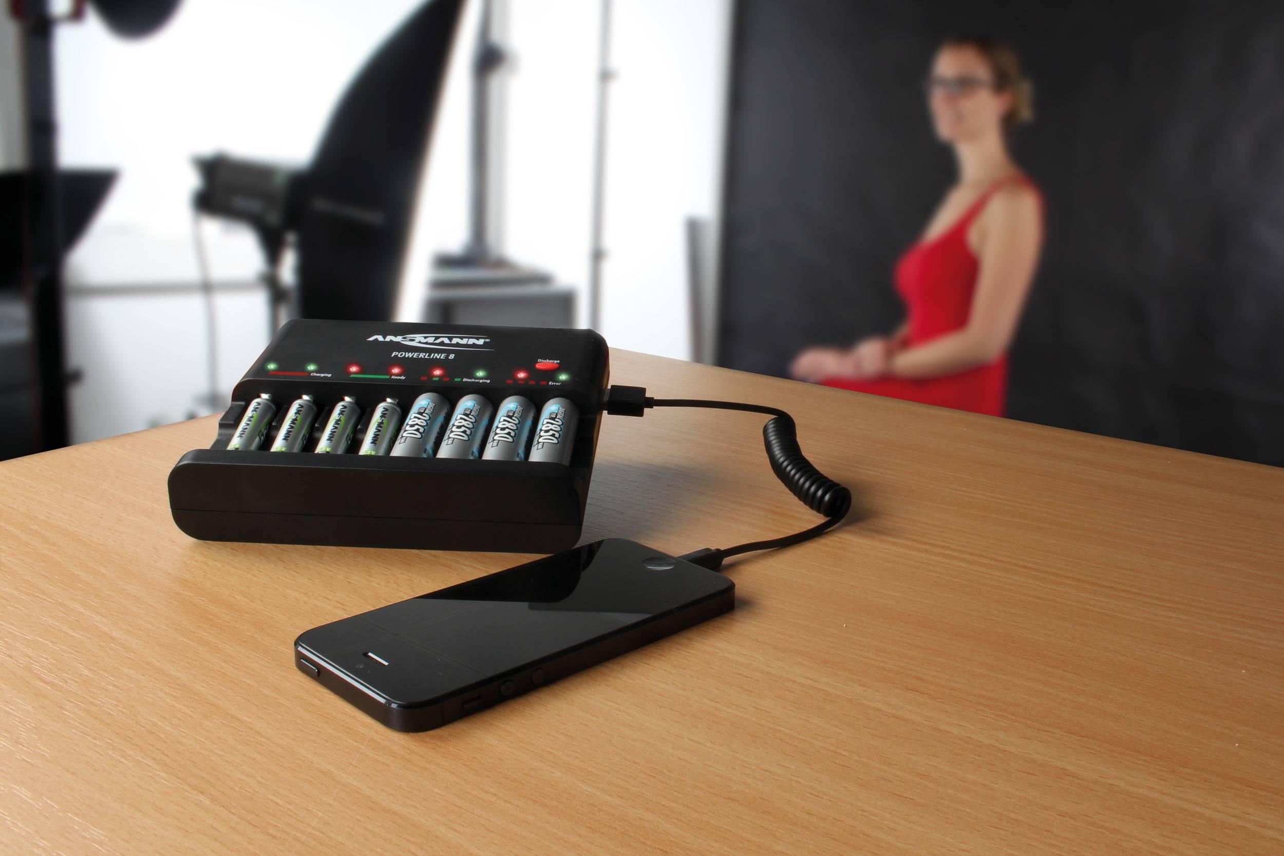 Eine Akkuladestation, die Batterien auflädt, ist mit einem Smartphone verbunden. Im Hintergrund steht eine unscharfe Person.