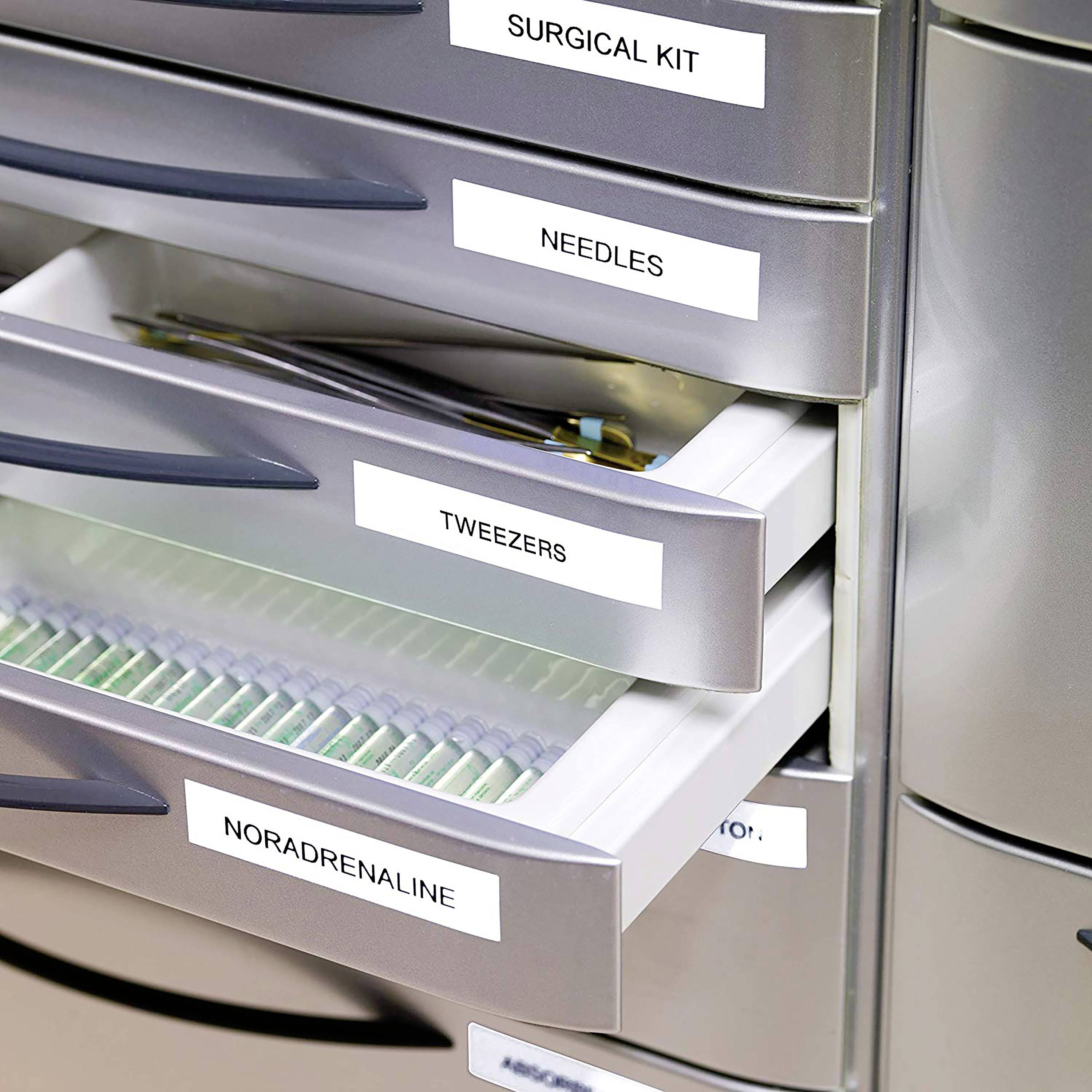 Medizinschrank mit geöffneten Schubladen, die bestückt sind mit chirurgischen Utensilien, Nadeln, Pinzetten und Noradrenalin.